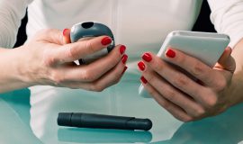Woman using phone and blood glucose meter to manage diabetes treatment