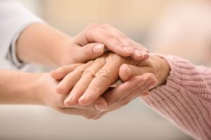 Nurse holding hands of elderly woman against blurred background